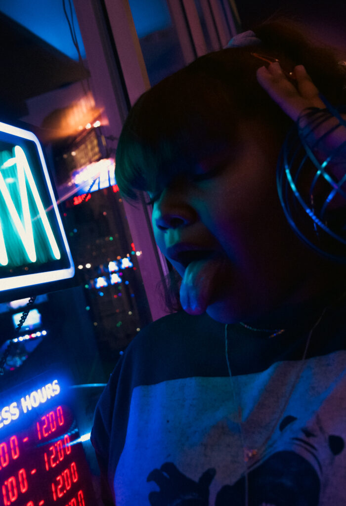 girl posing in front of neon sign with headphones